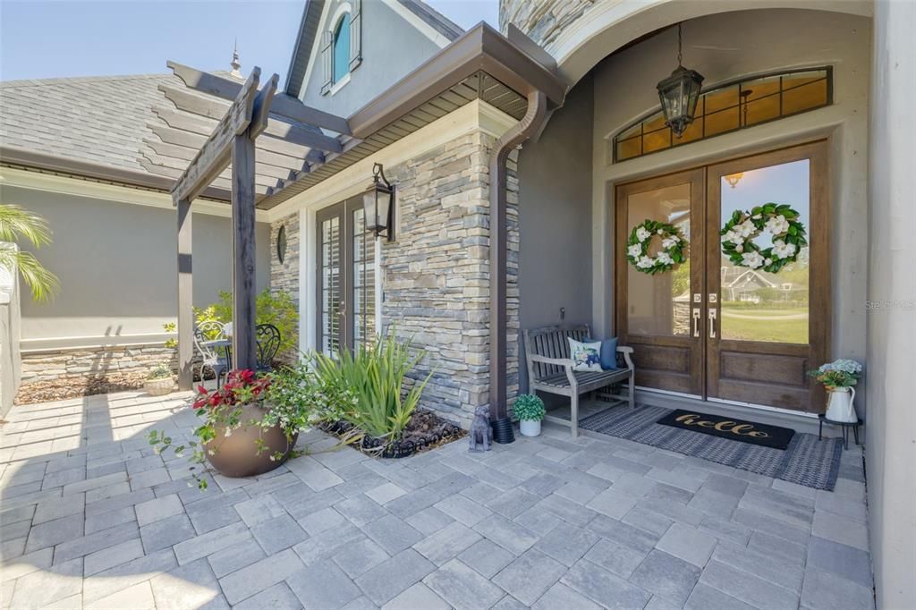 Double door covered front entry, pergola to the left patio to the right