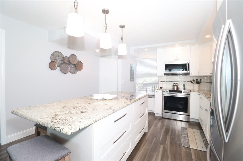 Stunning renovated kitchen. Granite island, seating, drawers for storage, Stainless appliances. Door and window with blinds lead to the walkway