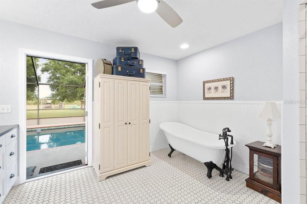 Owners ensuite bathroom featuring a clawfoot tub, walk-in enclosed shower, and direct access to the screened-in lanai and heated pool.