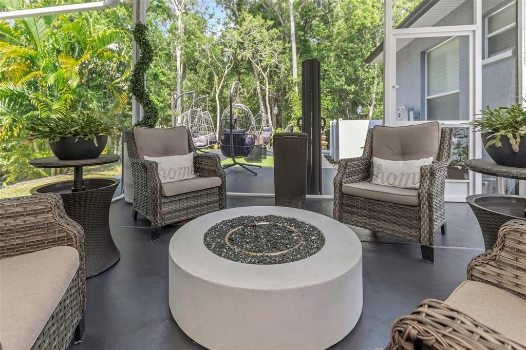 View of the expansive covered lanai with outdoor kitchen and additional seating with lighted gas burning center table. Notice the lovely wooded view