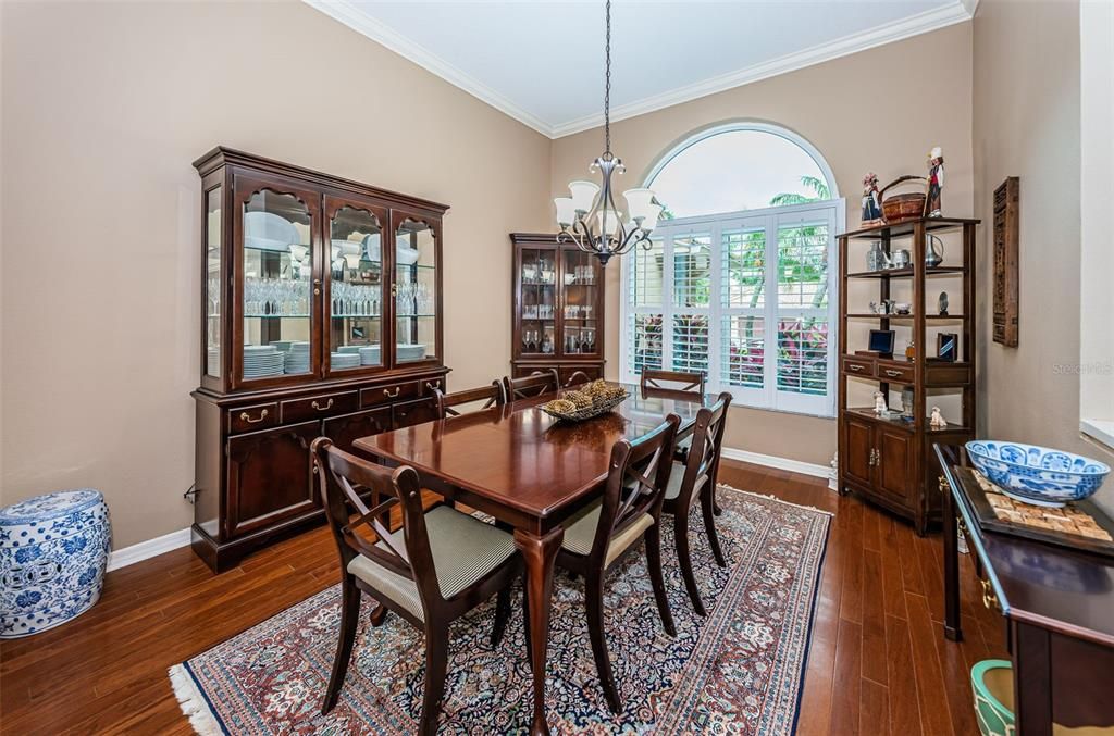 Formal dining with wood flooring, crown molding, & plantation shutters