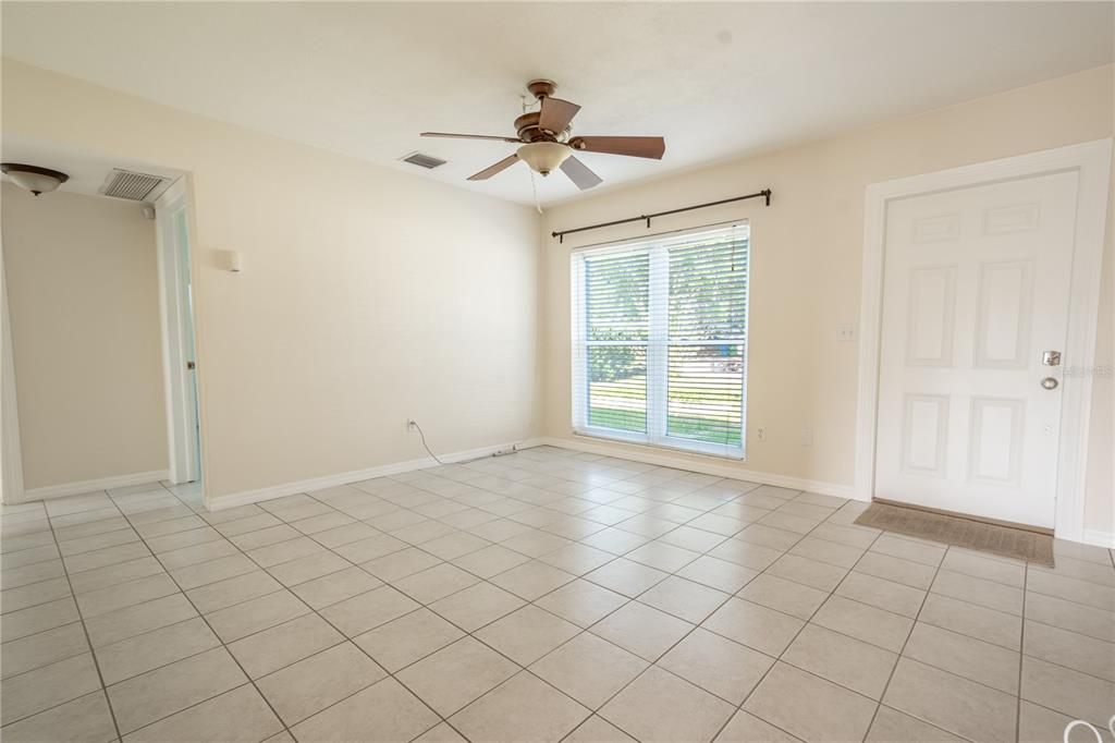 Large neutral toned living room, with picture window, ceramic tile flooring and ceiling fan.