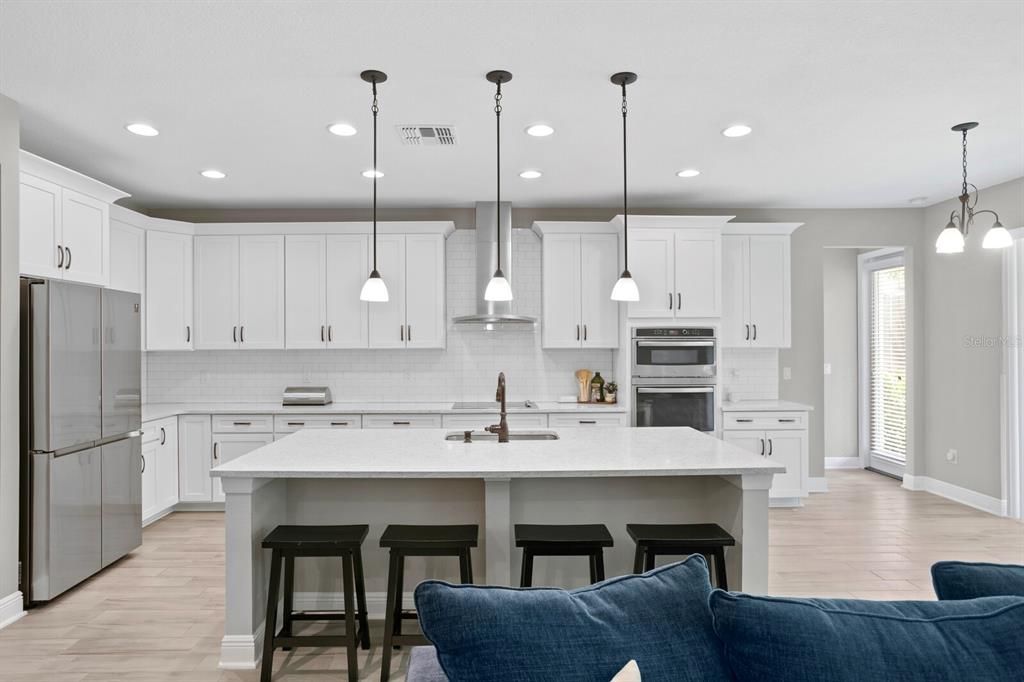 Island seating for 4, adorned by quartz countertops throughout, pendant lighting, space for a dinette area.