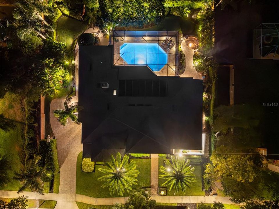 Aerial view with extensive landscape lighting and backyard oasis with solar heated pool and fire pit