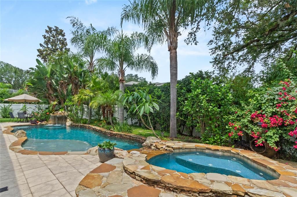 View of lagoon style pool with oversized hot tub, grotto paver patio and sun shelf.