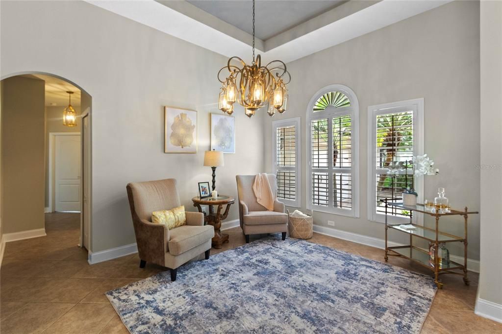 The sunny formal living room features a tray ceiling, custom lighting, wood shutters and plenty of space to receive guests.