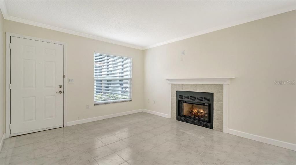 Great room featuring high ceilings, crown molding, a decorative brick fireplace, and tile flooring.