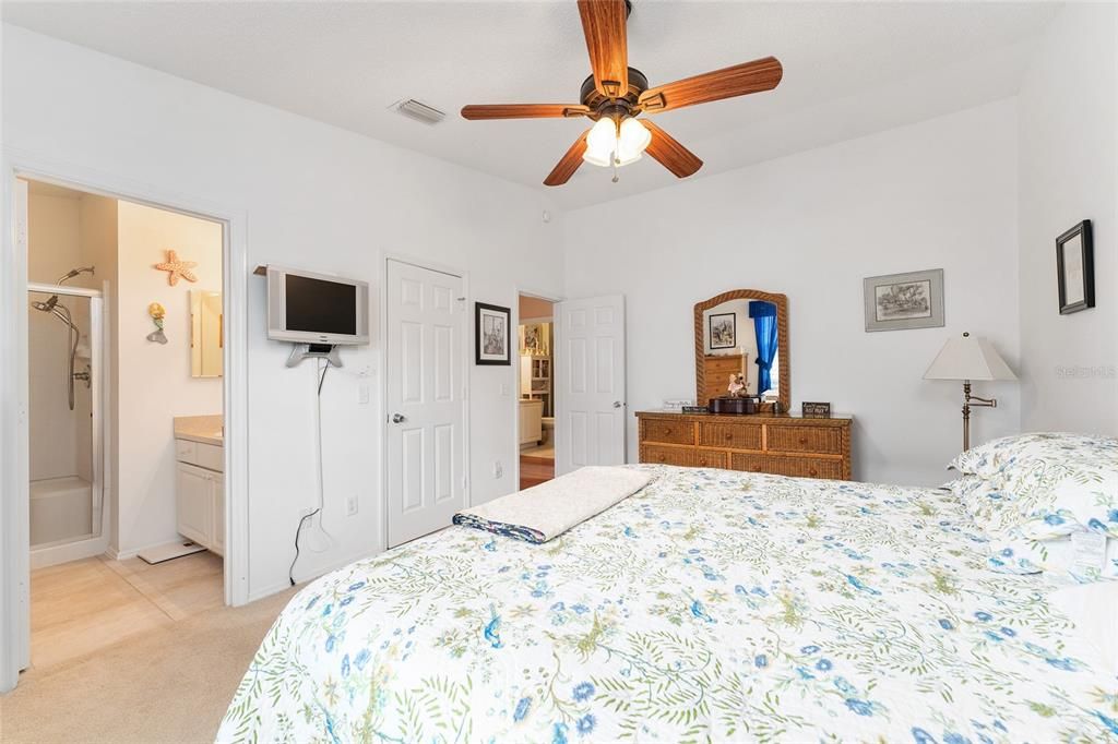 PRIMARY BEDROOM WITH WALL MOUNTED TV, LIGHTEC CEILING FAN, WALK IN CLOSET AND EN SUITE BATH.  FRAMED ART ON WALLS AND LINENS BELONG TO CURRENT RENTER.