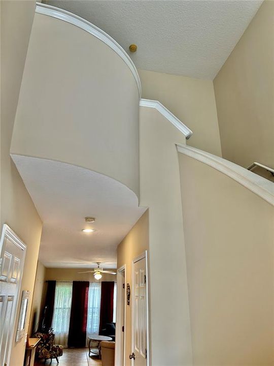 Foyer with soaring, curved stairwell, looking into the great room.