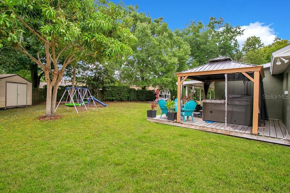 Outdoor Oasis with a storage shed, gazebo, playground, playhouse, wooden deck, mass producing mango tree and an avocado tree yet to bloom