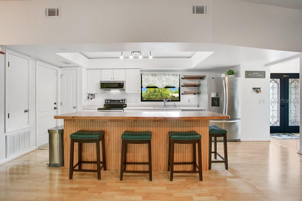 Kitchen features rustic floating shelves, an island with seating and cabinet storage, stainless steel appliances and updated lighting