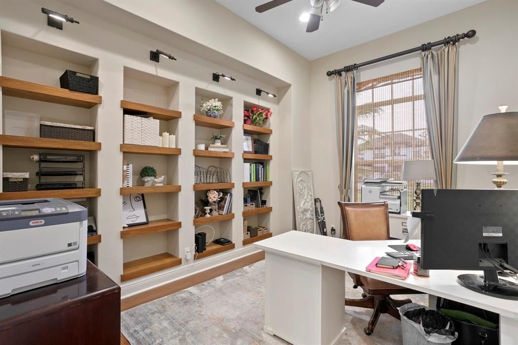 Office with hardwood floors and custom shelving and library lighting.