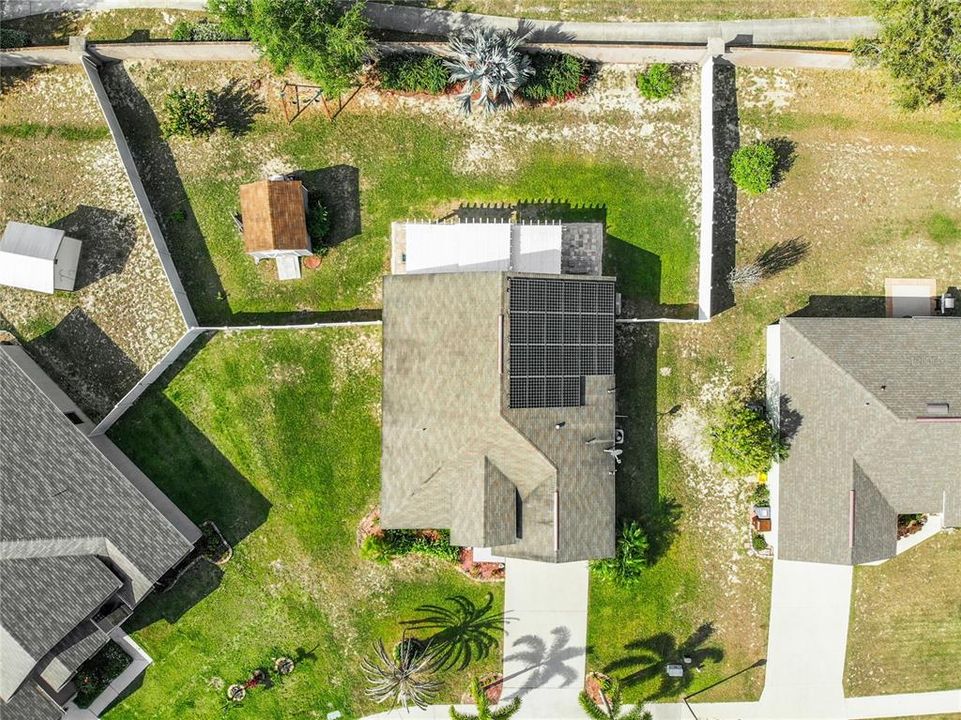 Aerial view shows solar system and fenced back yard with shed.