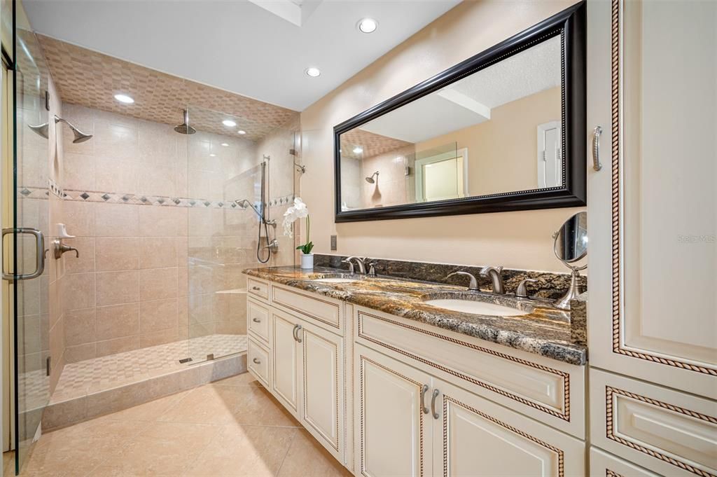 Primary ensuite bath with elegant custom cabinetry, granite, and oversized walk in shower