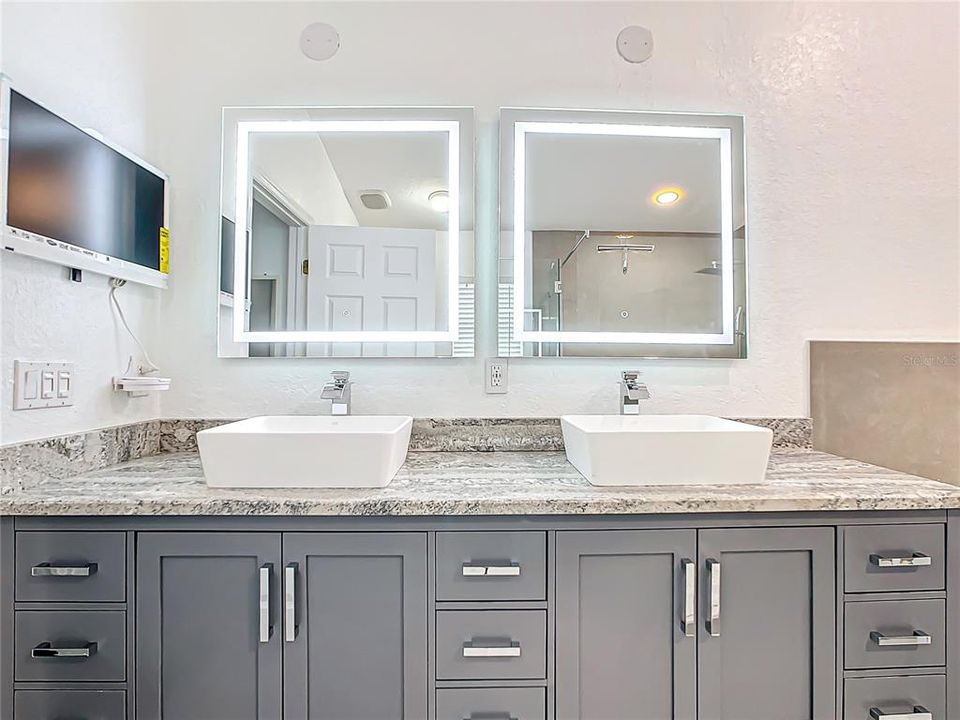 The En-suite primary bathroom has been beautifully remodeled with updated dual-vessel sinks, granite countertops, and illuminated defogging mirrors.