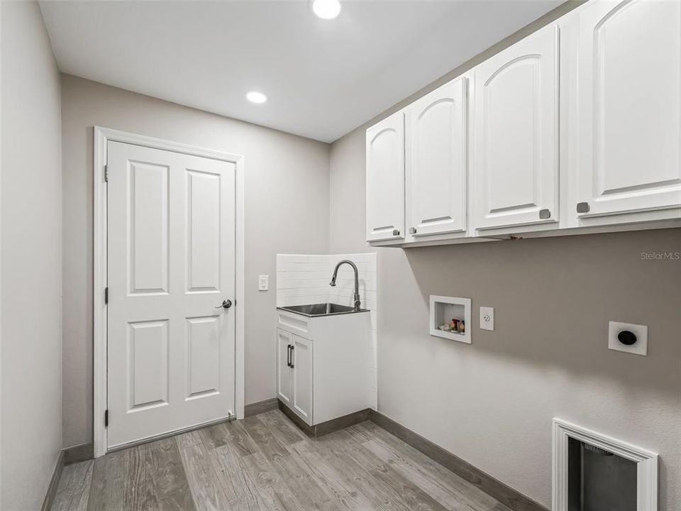 INTERIOR LAUNDRY ROOM WITH DOOR LEADING TO THE GARAGE. STORAGE CABINETRY AND NEW SET TUB SINK AND CABINET WITH BACK SPLASH