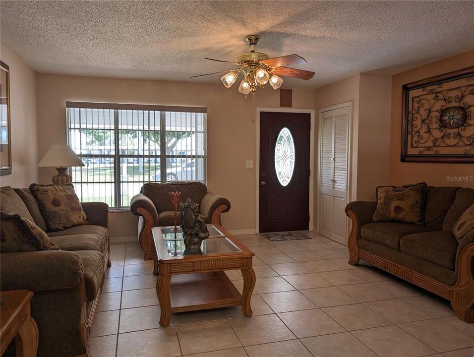 Living room features tile flooring, ceiling fan, neutral decor and coat closet at entry.