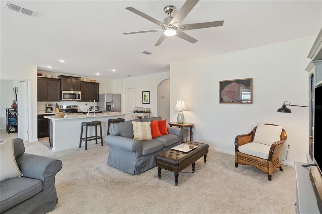 Family room with ceiling fan, kitchen in background