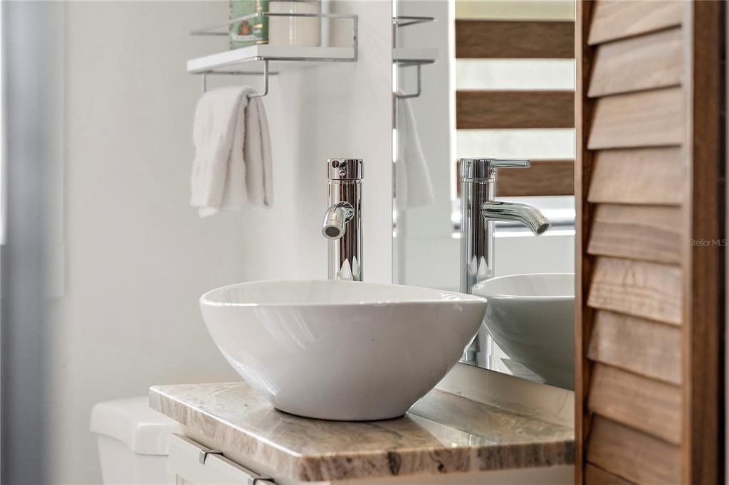 A vessel sink is perched atop stunning granite on a mirrored vanity with storage.