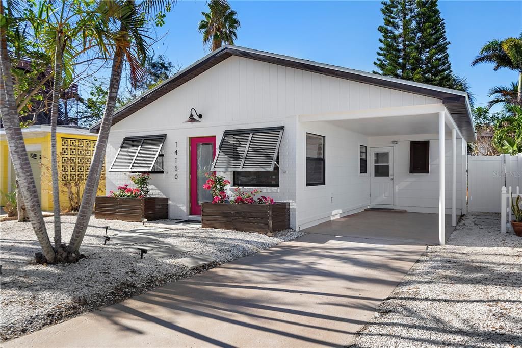 The front of the home features a covered carport, Refinished Epoxy driveway, tropical palms and Bahama Shutters providing this home with shade from the sun and insulation from the heat.
