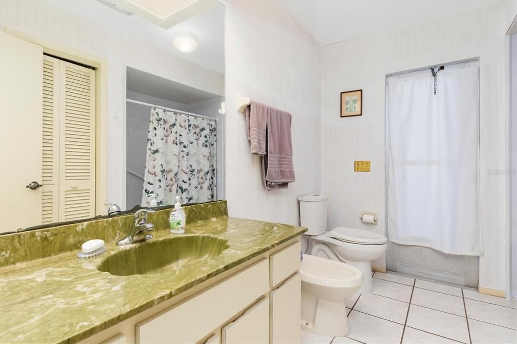 Guest bathroom with shower, long vanity, bidet, and door providing pool/sauna/lanai access.