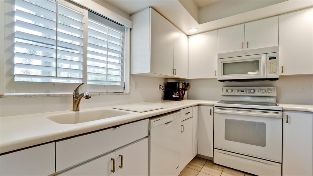 KITCHEN UPDATES INCLUDE A NEW STAINLESS REFRIGERATOR, CEILING FAN & LIGHTING, BERMUDA SHUTTERS & CORIAN WHITE COUNTERS