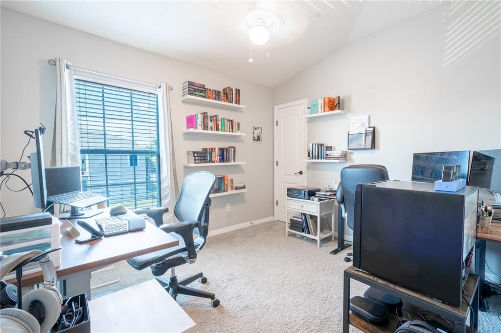 Bedroom 4 currently serves as a home office. It features a large built-in closet, plush carpet, shelving and a ceiling fan with light fixture.