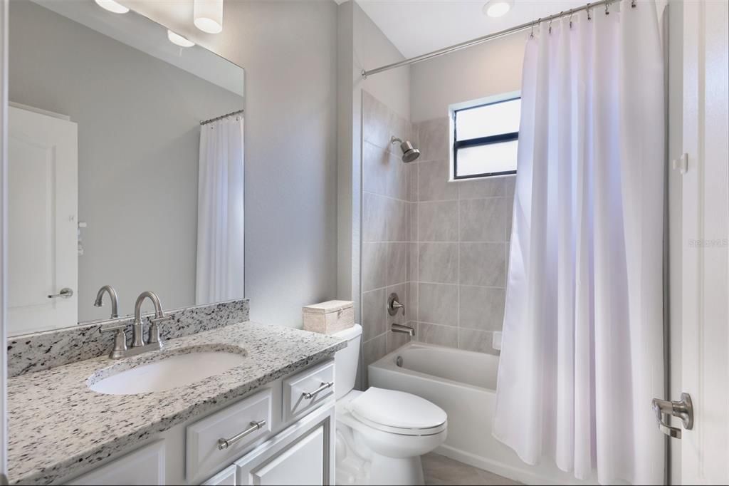 Guest bath has a linen closet and perfect size tub with a window above and large granite counter space