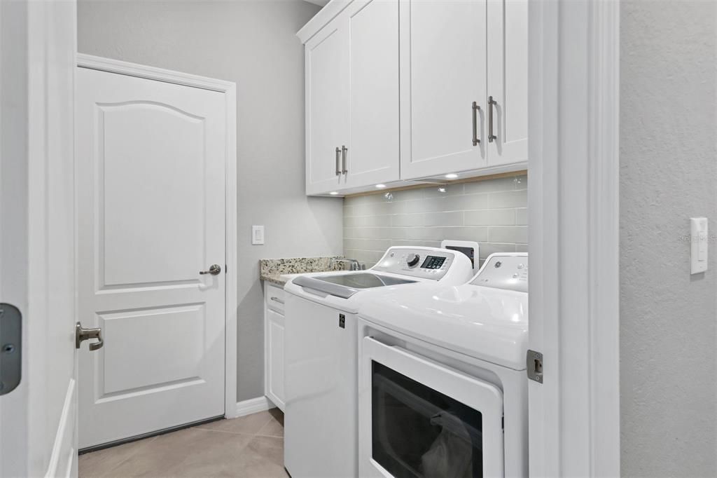 Laundry room has built-in cabinets with task lighting, laundry tub with granite counter, tile back splash wall and gas dryer.