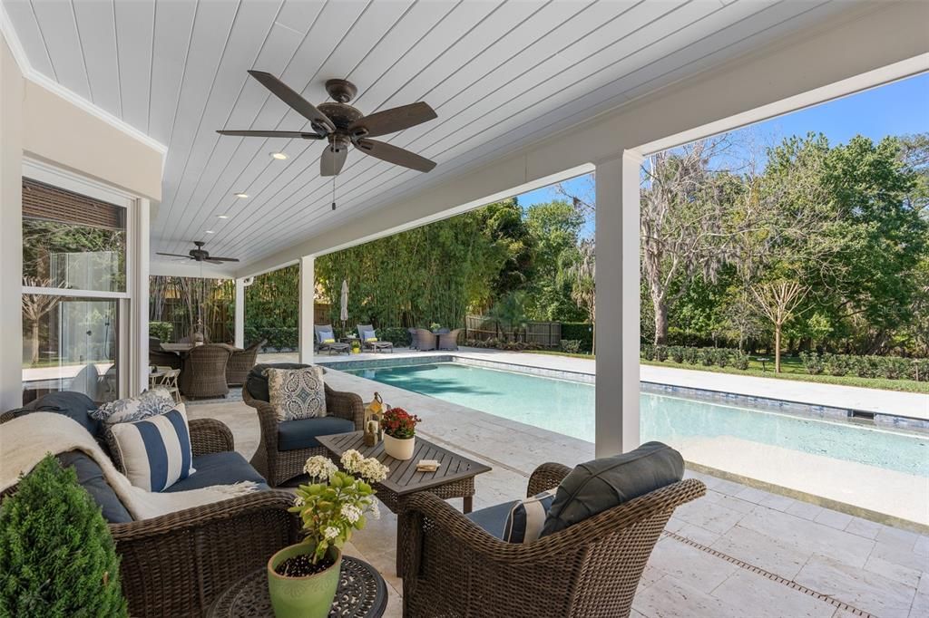 Outdoor lanai area with tongue and groove ceiling, travertine overlooking sparkling pool and expansive yard