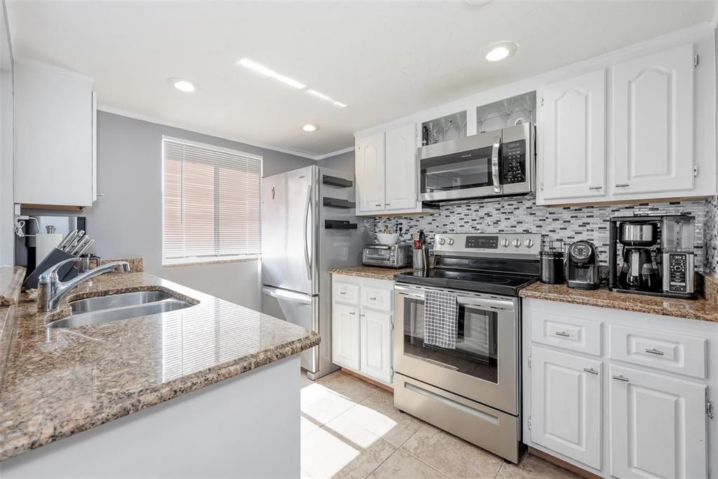 Kitchen featuring backsplash, light tile floors, sink, white cabinetry, and appliances with stainless steel finishes