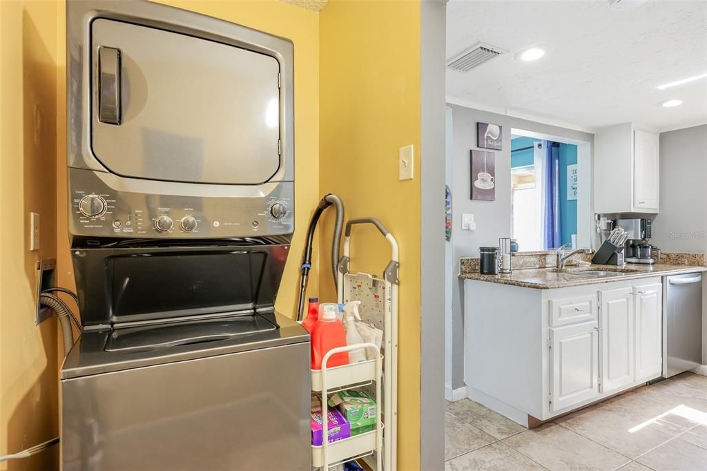 Clothes washing area featuring stacked washer / dryer, sink, and light tile flooring