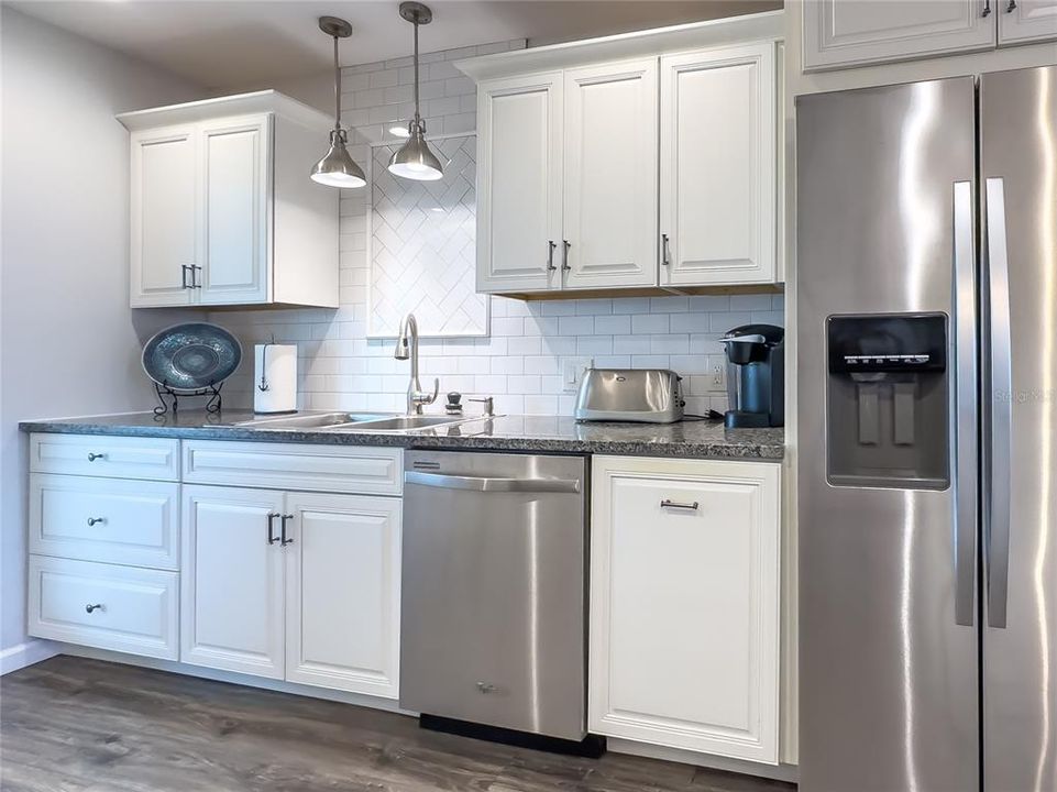 Stainless sink, faucet, tile backsplash, dishwasher & refrigerator with ice/water on the door.