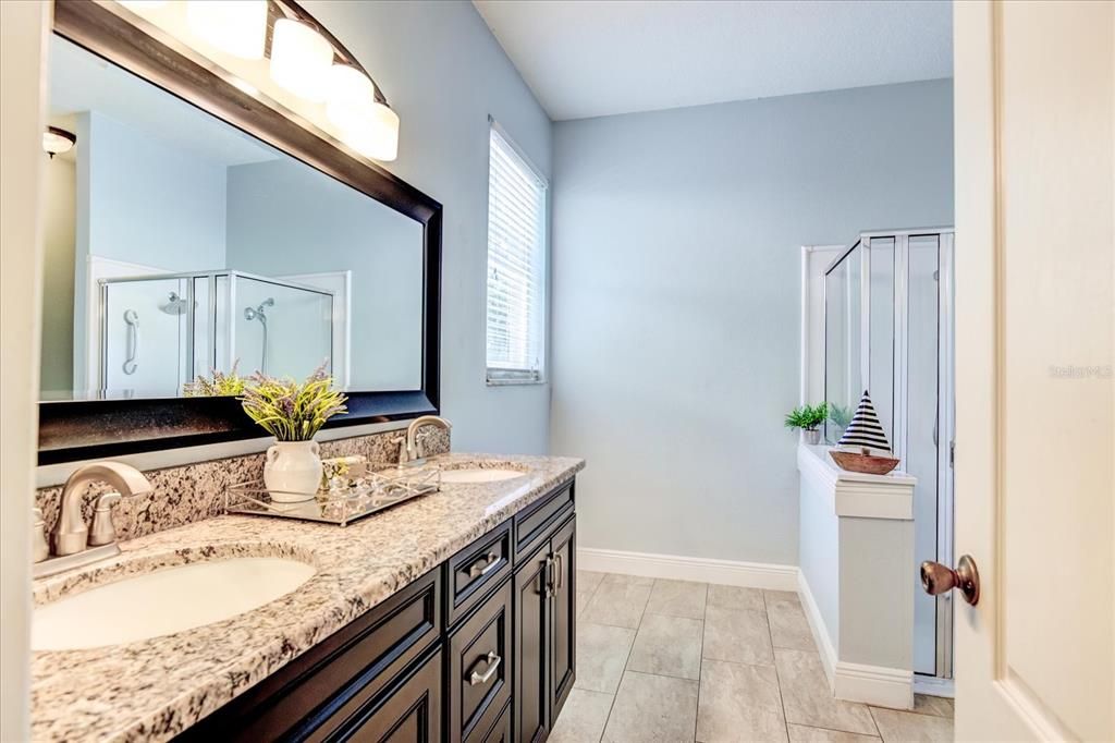 Primary bathroom with double sinks, granite countertops, and shower