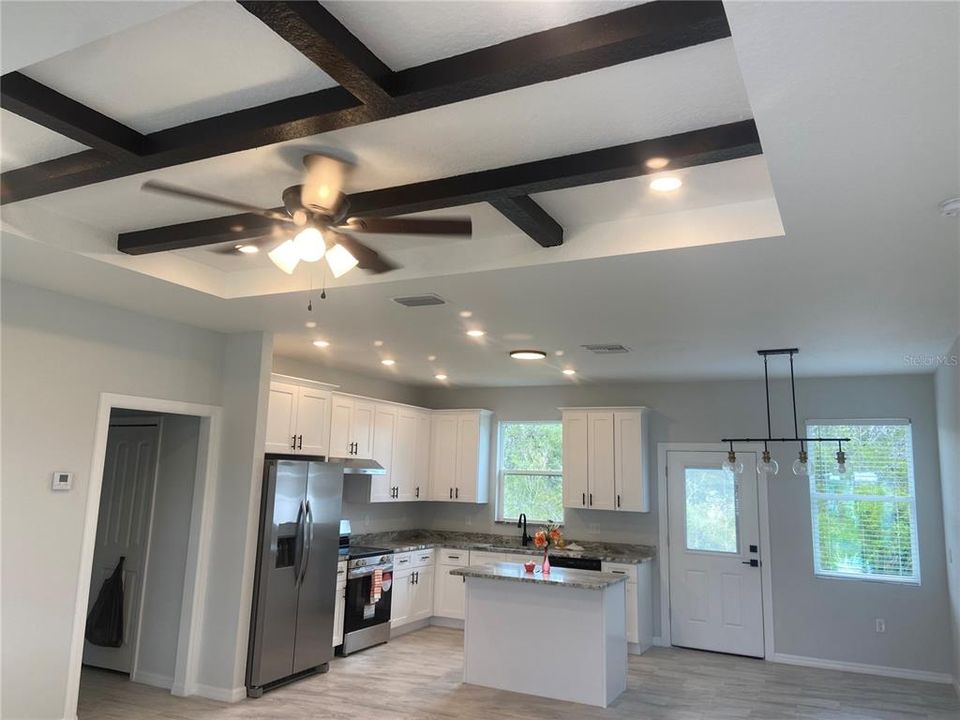 Great room with coffered ceiling, recessed lights to open kitchen