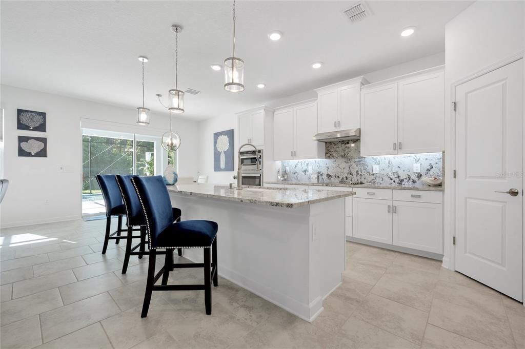 The gorgeous kitchen overlooks a casual dining space and generous family room complete with a stylish accent wall and sliding glass door access to the lanai, outdoor kitchen and HEATED/SCREENED POOL!