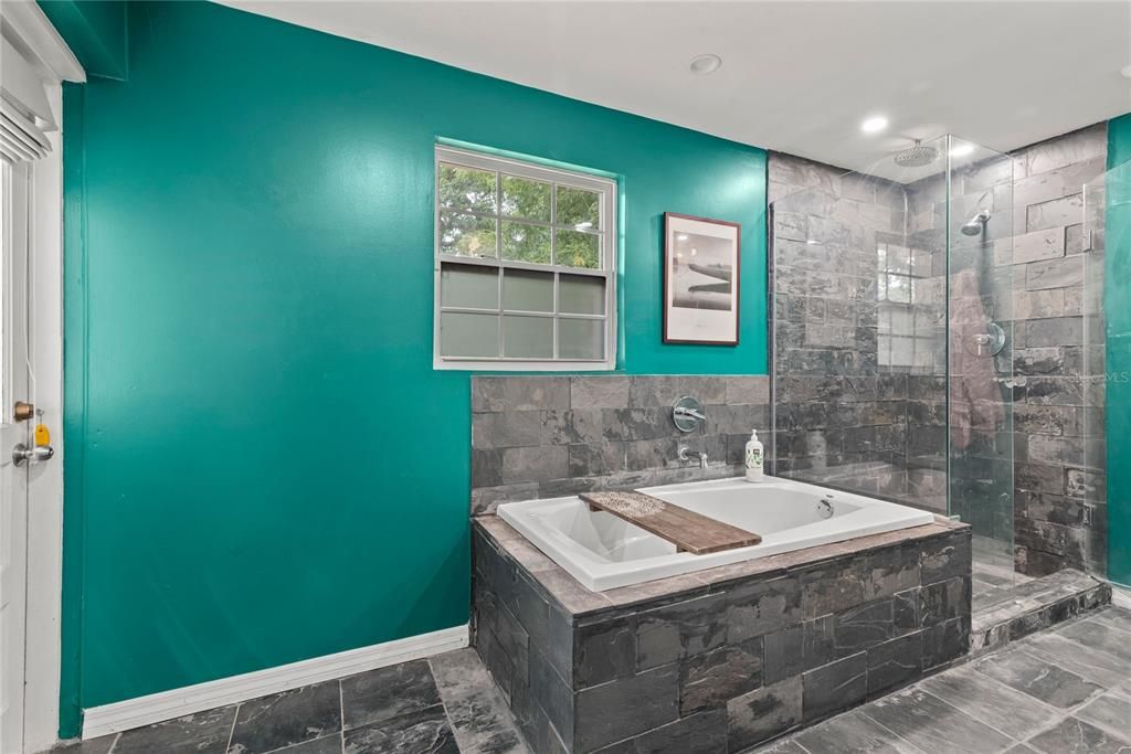 Jacuzzi tub and walk-in shower with glass walls and rain shower head.