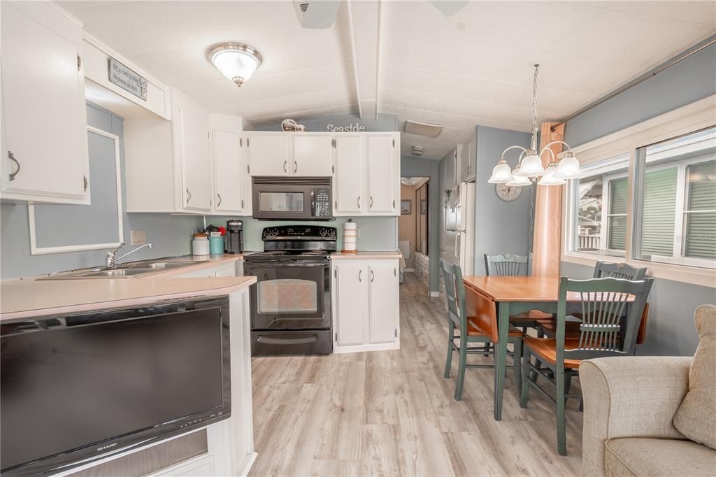 The kitchen features a range, a microwave and refrigerator. A chandelier hangs above the dining table.