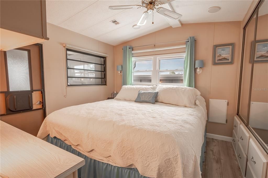 The bedroom features wood laminate flooring, built in cabinetry, a vaulted ceiling with ceiling fan and mirrored closet.