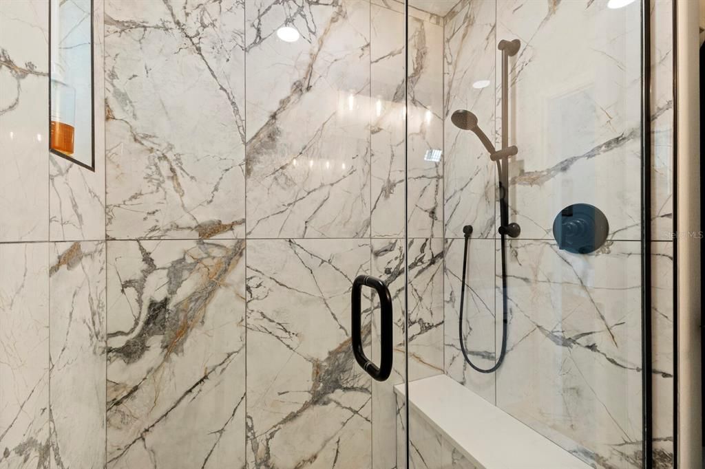 The natural stone tiled primary shower has a privacy window that lets in natural light.