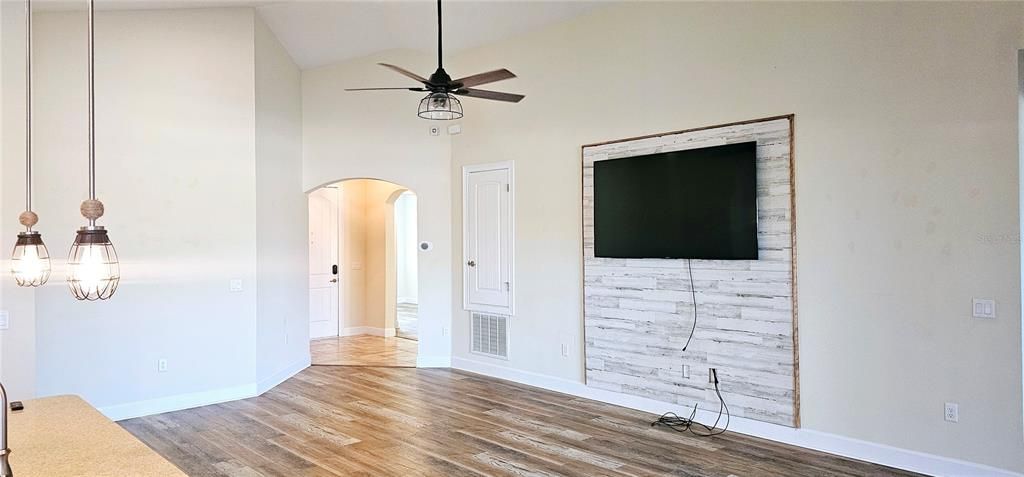 Open concept Great Room with vaulted ceiling with recessed lighting, ceiling fan, Luxury Vinyl flooring, and sliding doors leading to screened and paved Lanai.