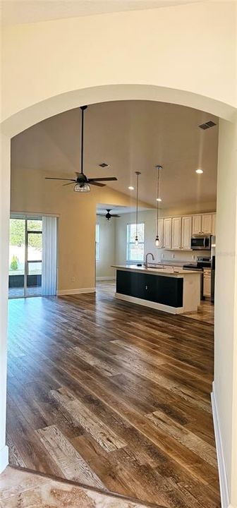 Front entry Foyer with decorative niche and view of open concept Great Room with vaulted ceiling with recessed lighting, ceiling fan, Luxury Vinyl flooring, and sliding doors leading to screened and paved Lanai.