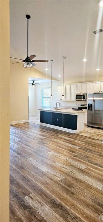 Open concept Great Room with vaulted ceiling with recessed lighting, ceiling fan, Luxury Vinyl flooring, and sliding doors leading to screened and paved Lanai.