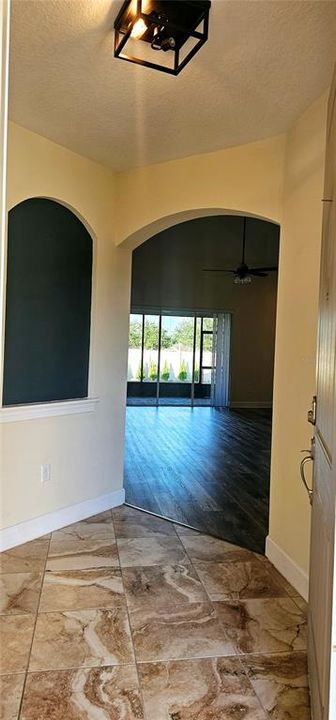 Front entry Foyer with decorative niche and view of open concept Great Room with vaulted ceiling with recessed lighting, ceiling fan, Luxury Vinyl flooring, and sliding doors leading to screened and paved Lanai.