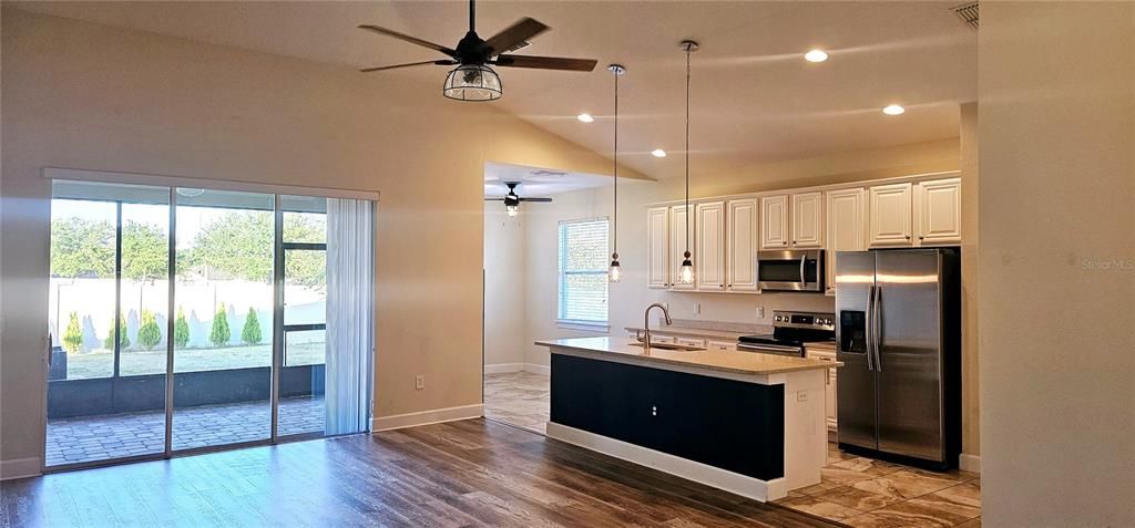 Open concept Great Room with vaulted ceiling with recessed lighting, ceiling fan, Luxury Vinyl flooring, and sliding doors leading to screened and paved Lanai.