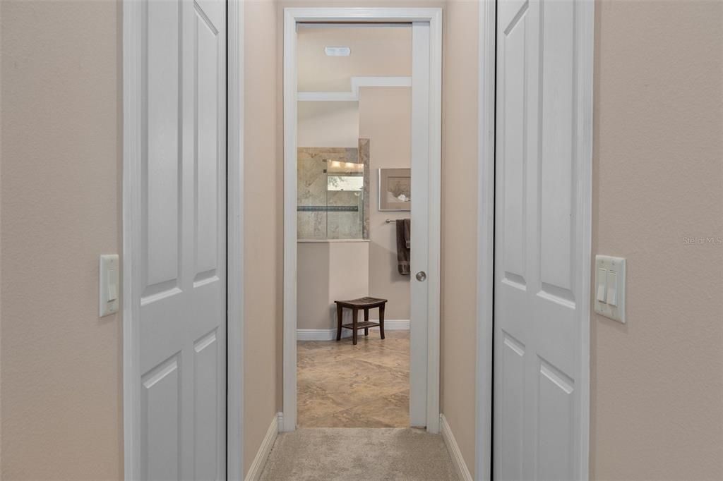 Hallway leading into Primary Bath is flanked by two walk-in closets, each with a pocket door.