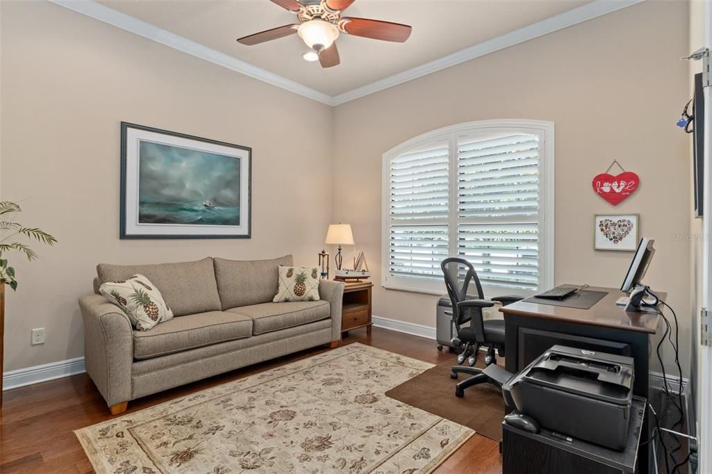 The den features crown molding, plantation shutters, and wood floors.