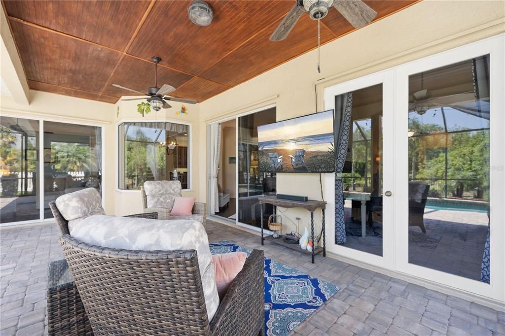 Brick paver lanai with wood paneled ceiling pocket glass sliding doors entering to main area of home and French doors leading to the primary bedroom.