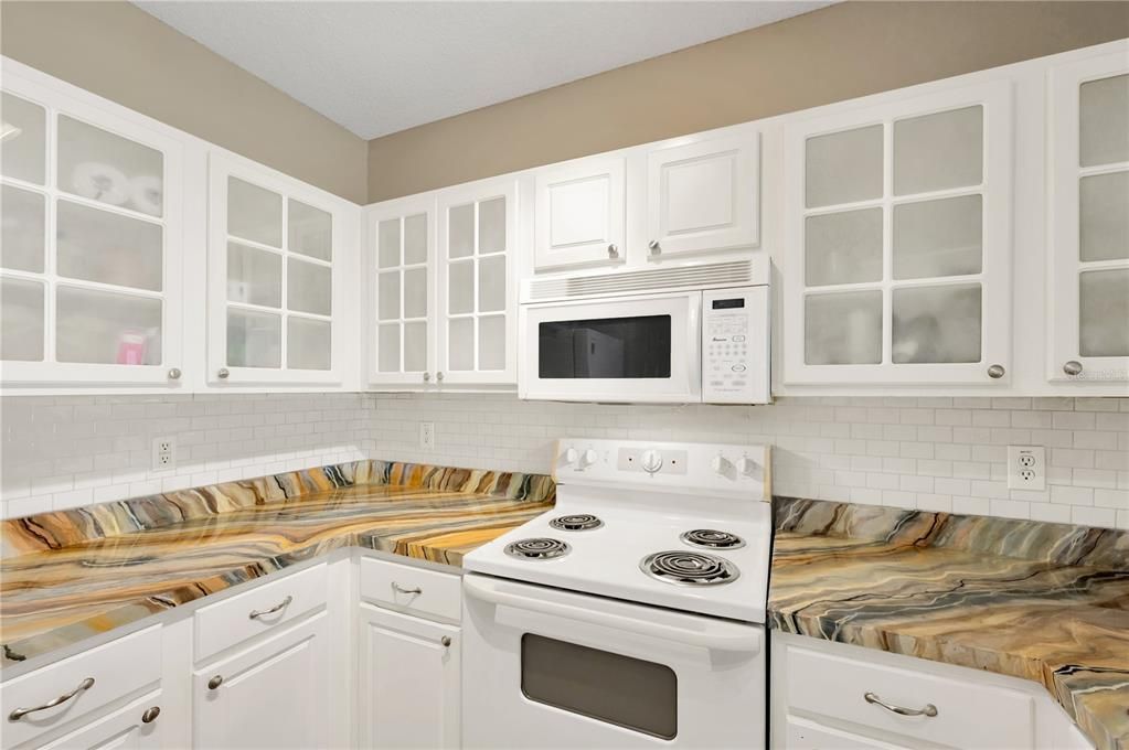 Kitchen features freshly painted white cabinetry with stylish glass inserts that obscure the contents inside and upgraded appliances (2024).