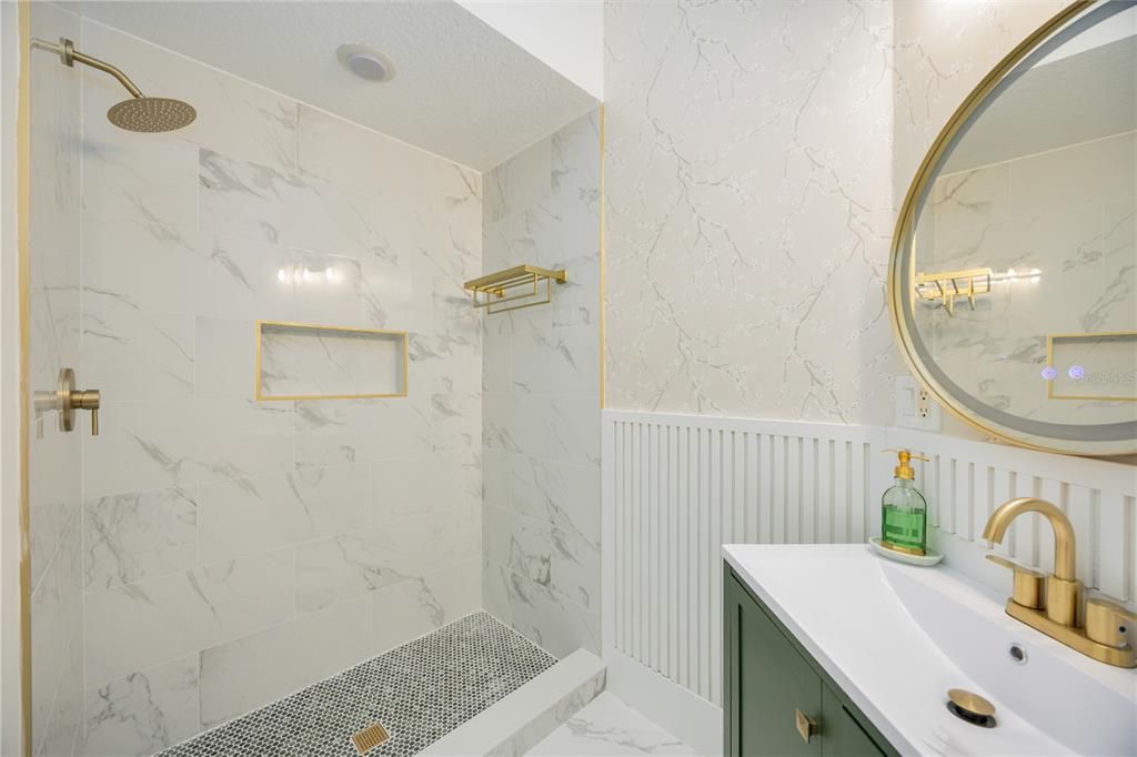 Guest bathroom features emphasizes luxury living with gold accented rainfall shower head and shower niche.